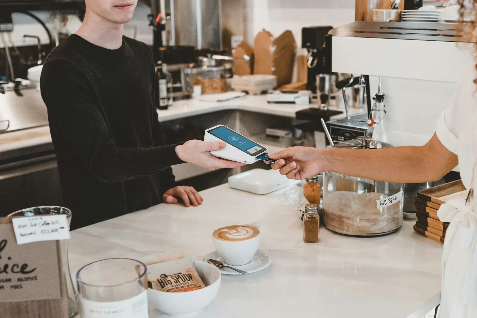 A customer paying at a cafe counter by tapping a card on a handheld payment terminal.