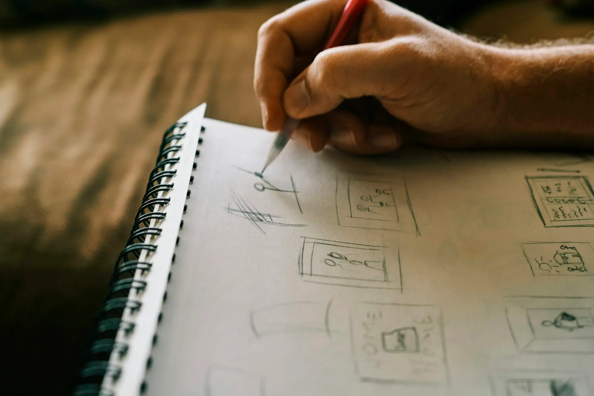 A hand sketching boxes and a flow of options in a spiral notebook on a wooden table.